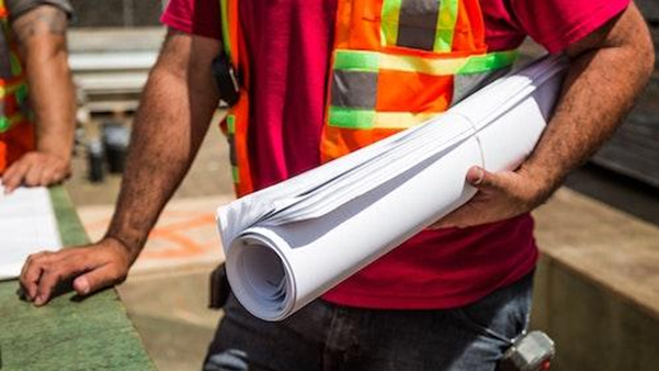 Construction worker in safety vest holding rolled blueprints on site