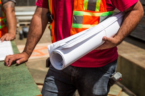 Construction worker in safety vest holding building blueprints